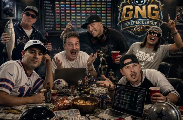 GNG Keeper League managers gathered around a chaotic fantasy football draft table with laptops, trophies, helmets, snacks, and a draft board in the background.